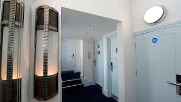 A hotel hallway with a blue carpet, a white door with a blue sign, and a wall-mounted light fixture.