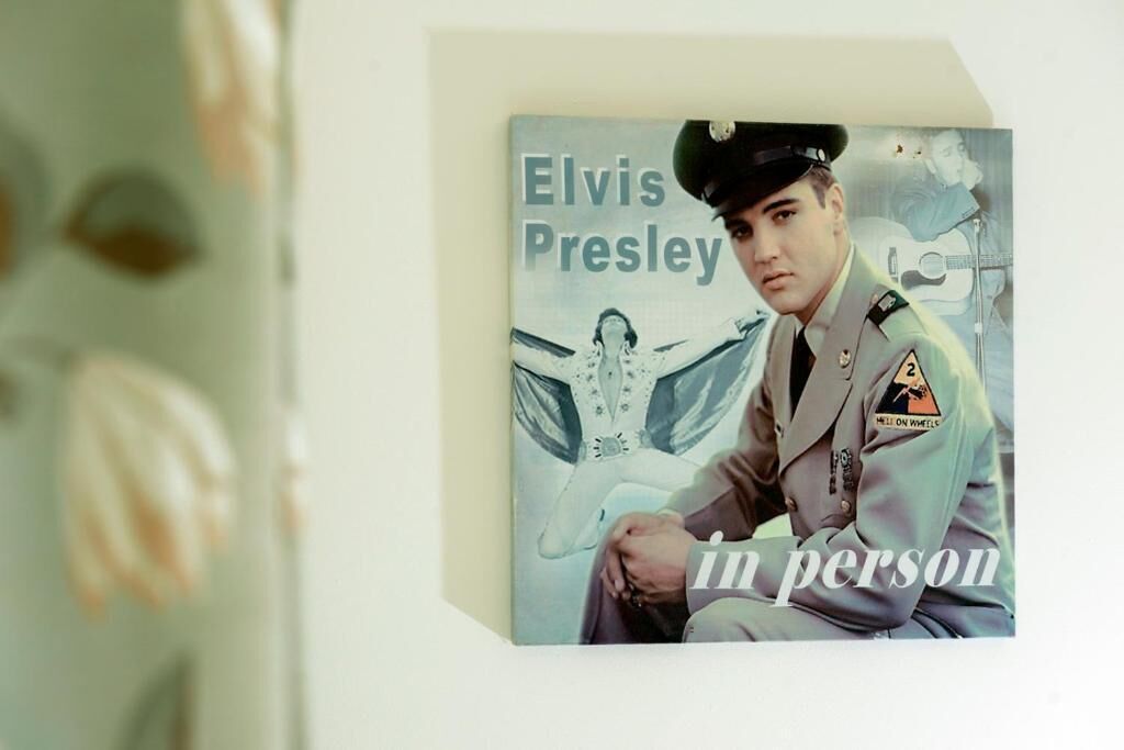 Portada de álbum enmarcada de Elvis Presley titulada 'In Person', con un uniforme militar y una guitarra de fondo.