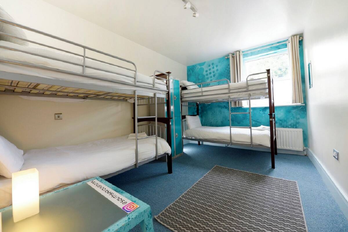 A room with bunk beds, a small table with a lamp, and a window with curtains.