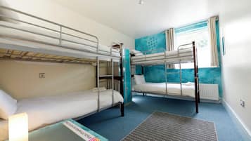 Una habitación con literas, una pequeña mesa con lámpara y una ventana con cortinas.