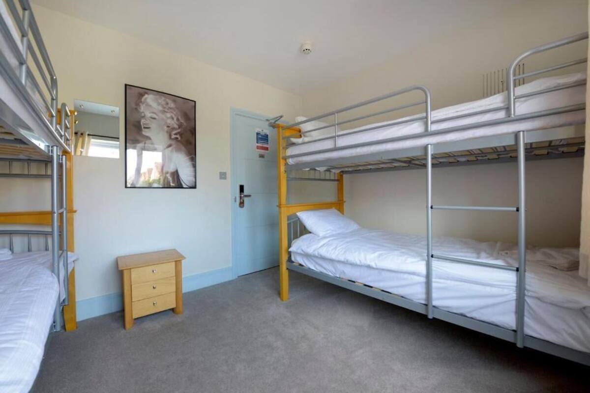 A dormitory room with bunk beds, a small wooden nightstand, and a poster on the wall.