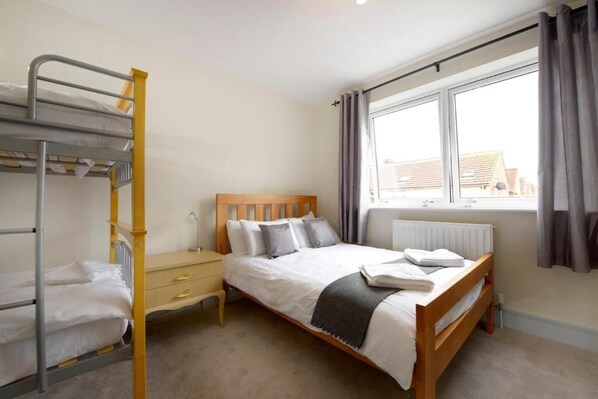 A bedroom with a bunk bed, a single bed, a bedside table, and a window with curtains. - Southsea Rocks Hotel (Portsmouth)