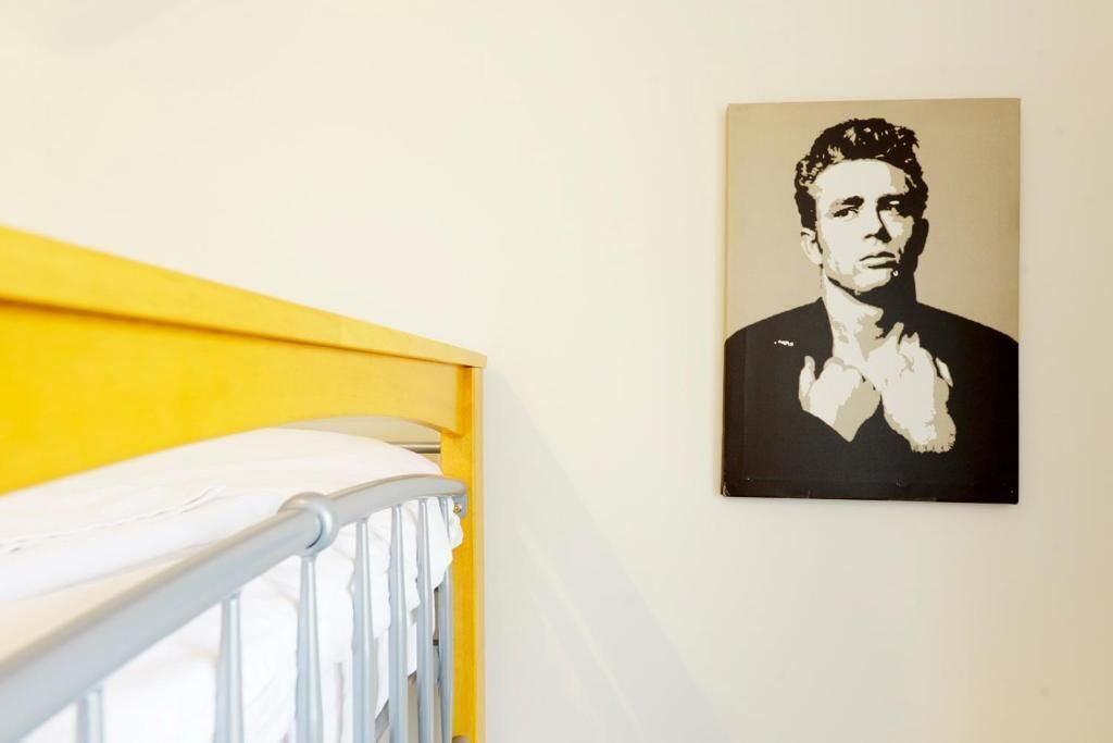 A room with a yellow headboard, a white crib, and a black and white portrait on the wall.