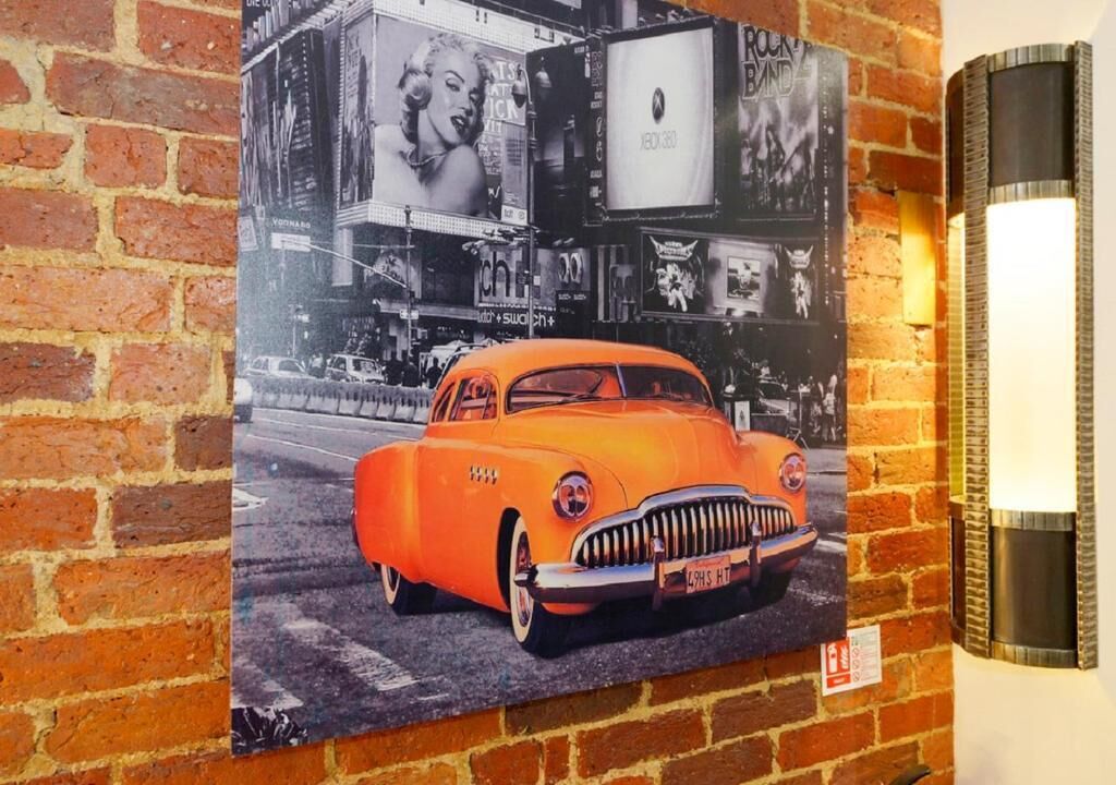 A vintage car poster on a brick wall with a modern light fixture beside it.
