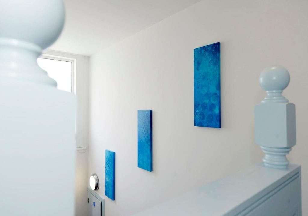 A bathroom with a white vanity, a white pedestal, and three blue artworks on the wall.