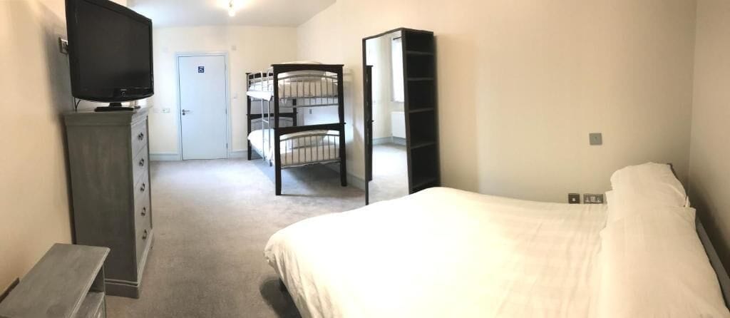 Una habitación de hotel con una cama, un aparador, un televisor, camas literas y una puerta.