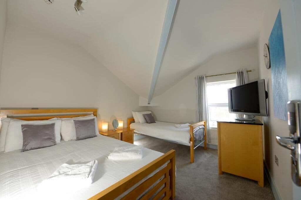 A bedroom with a large bed, a smaller bed, a TV, and a window with curtains.