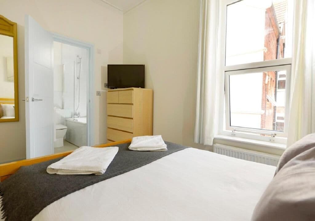 A hotel room with a bed, a television, a wardrobe, and a window with a view of buildings.