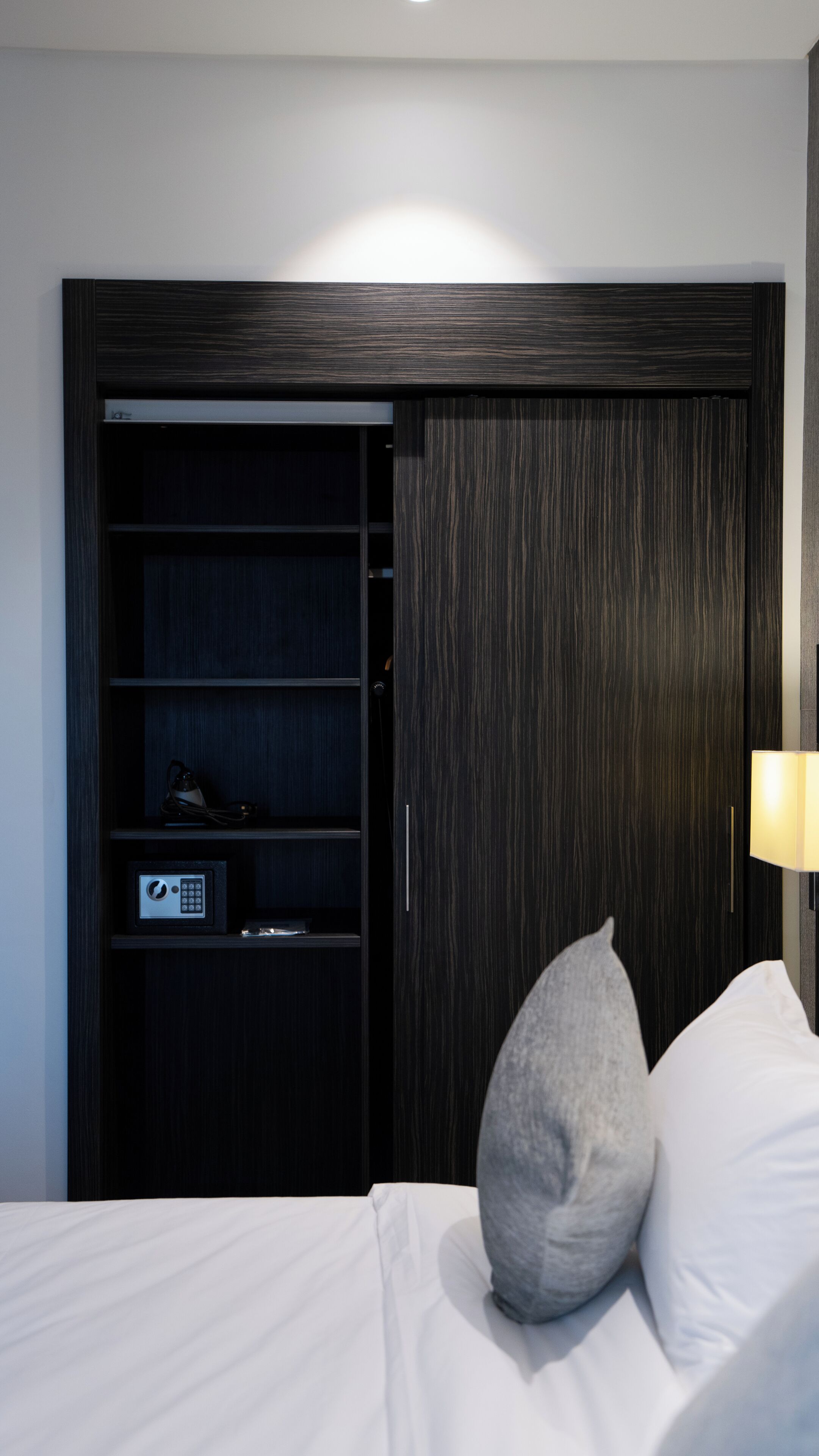 A hotel room with a bed, a nightstand, a lamp, and a wardrobe with a built-in safe.