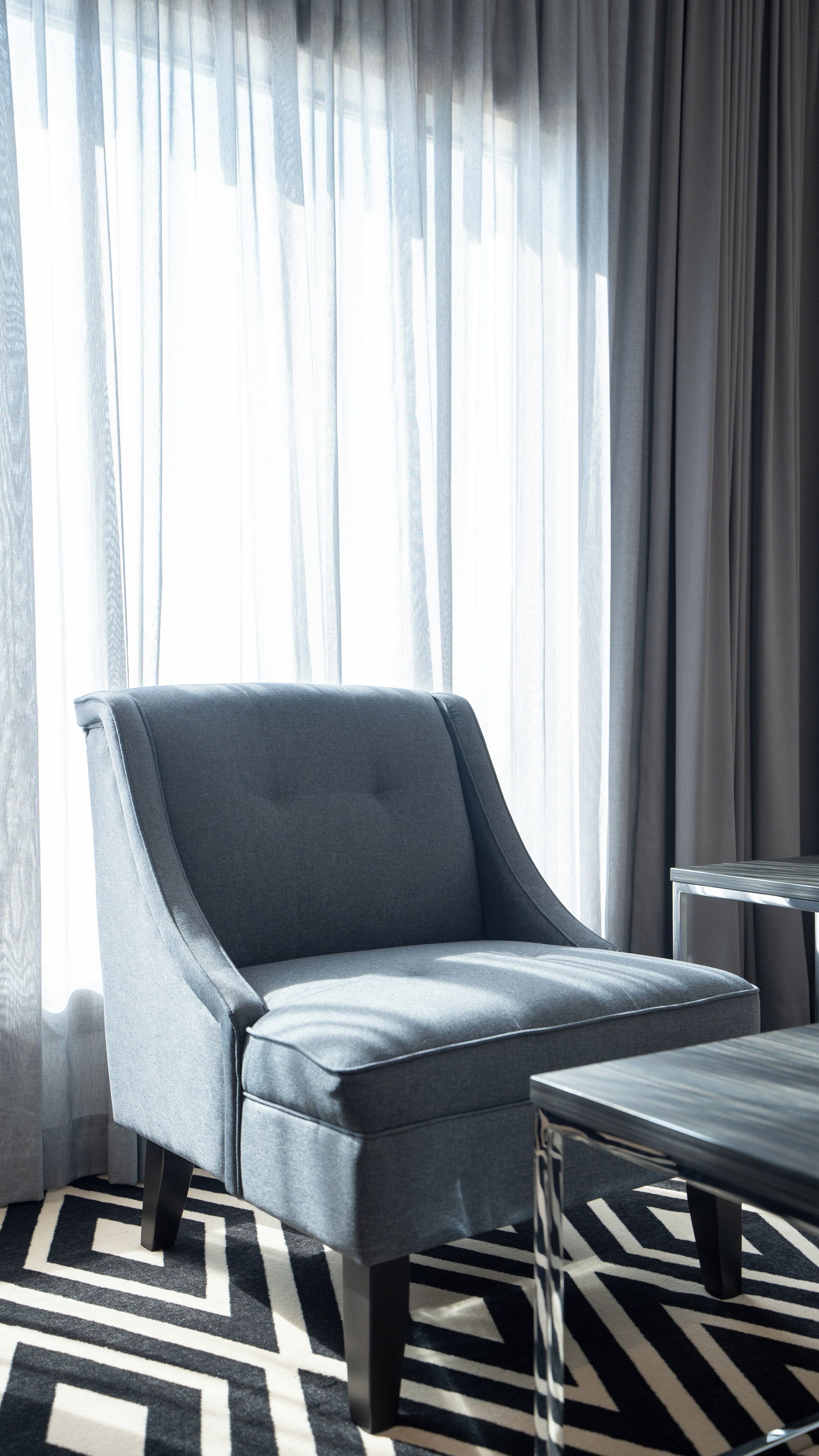 Un salon moderne avec un fauteuil gris, un tapis à motifs noir et blanc et une table d’appoint.