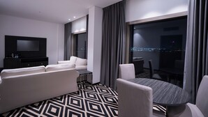 Une chambre d’hôtel moderne dotée d’un grand lit, d’un coin salon avec un canapé et des fauteuils, d’une petite table et d’un téléviseur.