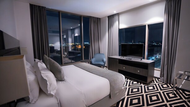 Une chambre d’hôtel moderne dotée d’un grand lit, d’un bureau avec une télévision et offrant une vue sur la ville grâce à de grandes fenêtres.