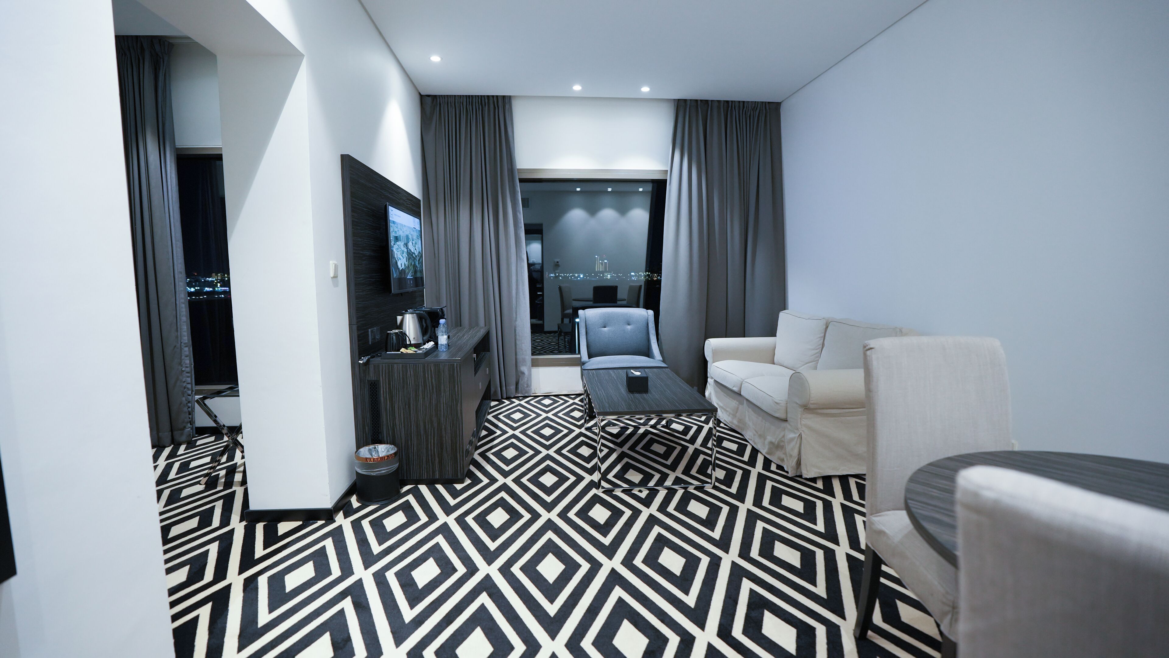 A modern living room with a geometric patterned floor, a sofa, a coffee table, and a TV mounted on the wall.