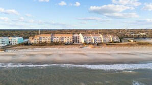 Un hotel frente a la playa con varias construcciones, una playa de arena y cielo despejado.