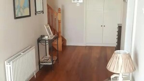 Ein Flur mit Heizkörper, einem Tisch mit Laptop, einer Lampe und einer Tür mit Fenster.