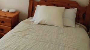 Ein Bett mit weißer Bettdecke und zwei Kissen, ein Nachttisch aus Holz mit einer Lampe und eine Wand mit einem Holzkopfende.