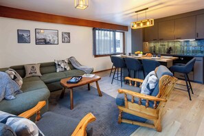 A modern living room with a sofa, chairs, a coffee table, and a kitchen area with bar stools.