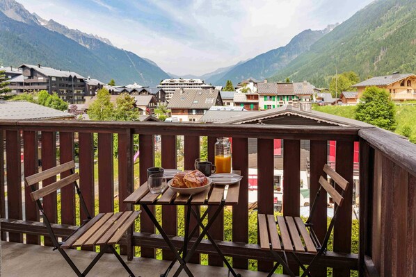 A wooden deck with a table set for breakfast, overlooking a mountain village with traditional buildings.