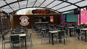 A strip shack with tables and chairs, a sign with a cartoon chicken, and a menu board. - Highfield Grange Holiday Park (Clacton-on-Sea)