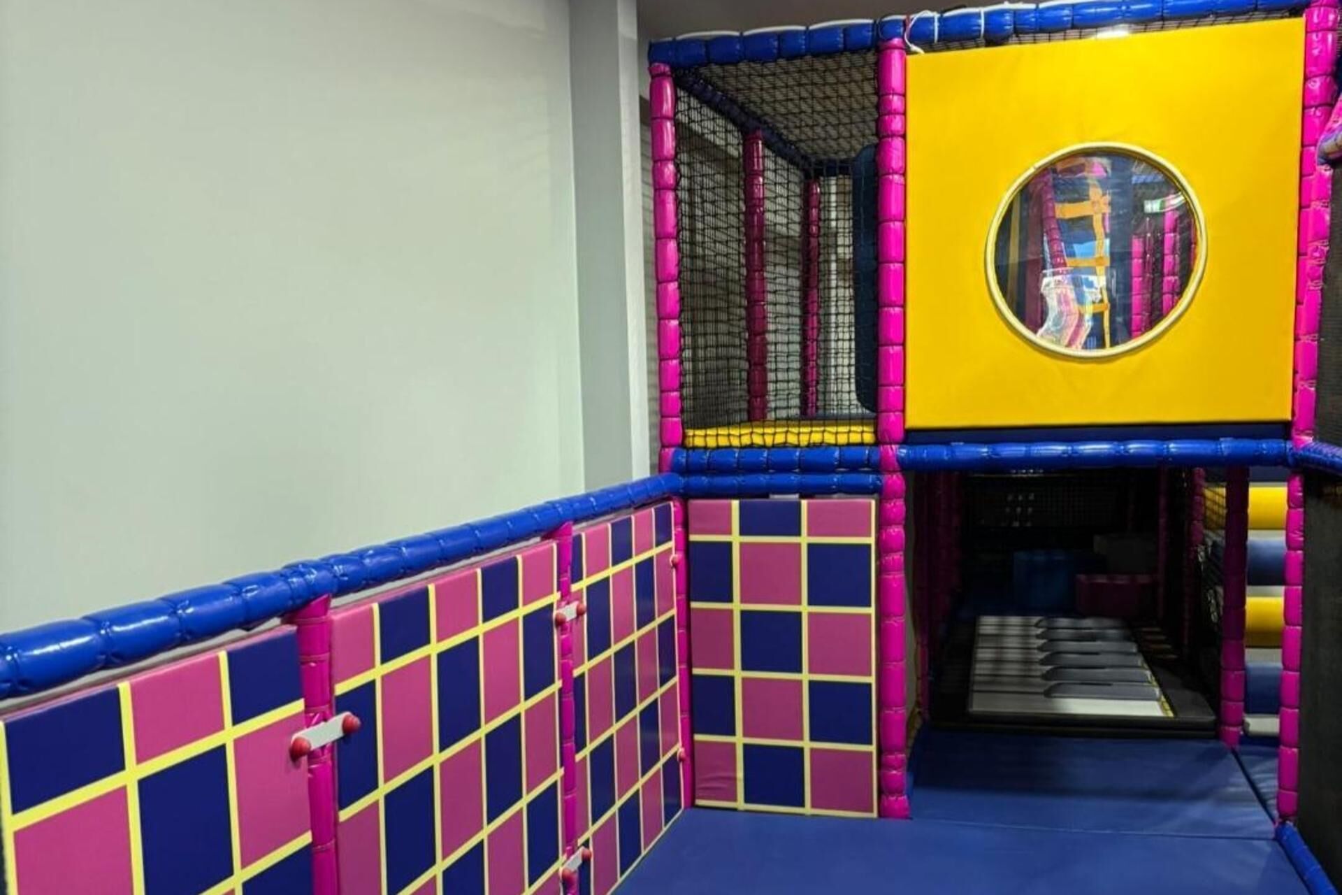 Un espace de jeux intérieur coloré, doté d’une zone d’escalade avec des filets et d’une fenêtre circulaire permettant d’observer l’espace.