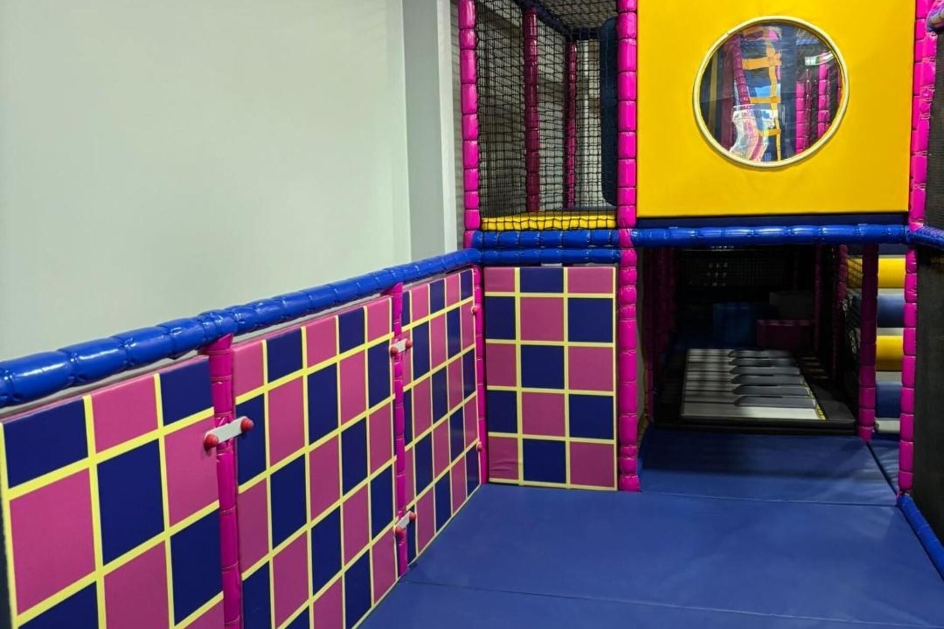 Un'area giochi interna dai colori vivaci, con pavimento blu, pareti rosa e azzurre e soffitto giallo.