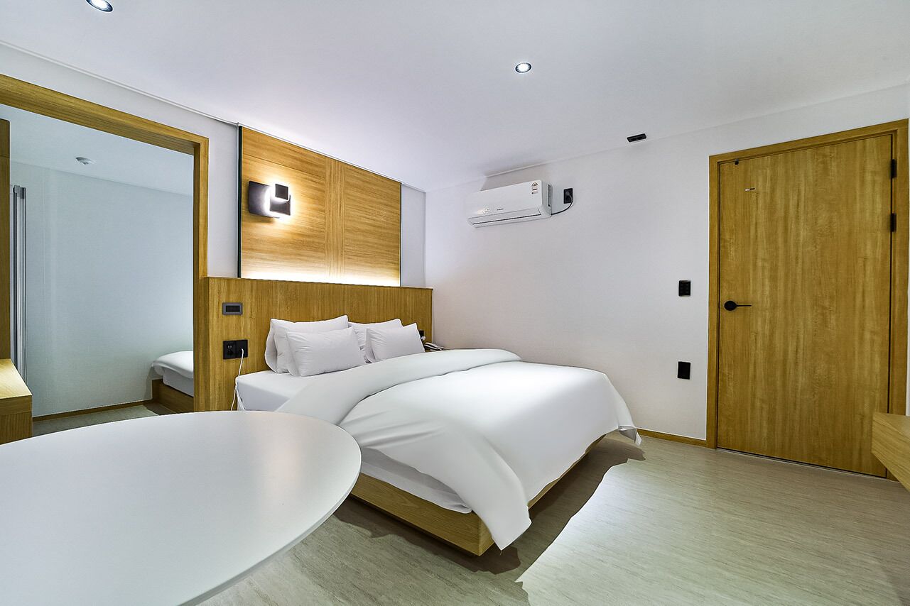 A modern hotel room with a large bed, a bedside table, a mirror, and a wooden wardrobe.