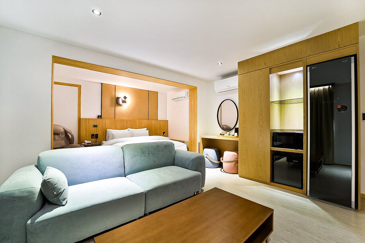 Una habitación de hotel moderna con sofá, una mesa de centro de madera, una cama con cabecero, un armario y un espejo.