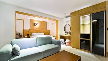 Una habitación de hotel moderna con sofá, una mesa de centro de madera, una cama con cabecero, un armario y un espejo.