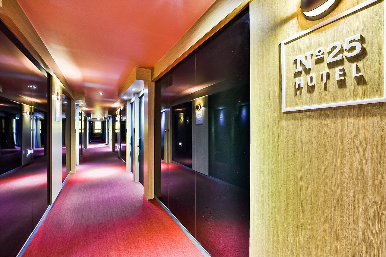 A hotel corridor with a red carpet, mirrored walls, and a sign reading "No 25 Hotel".