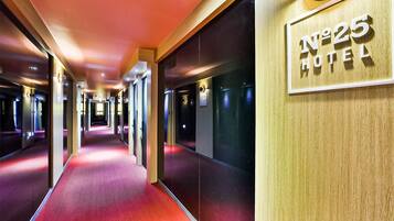 A hotel corridor with a red carpet, mirrored walls, and a sign reading "No 25 Hotel".