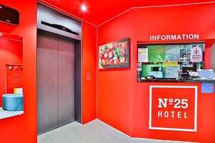 Vestíbulo de hotel con pared roja, un ascensor, mostrador de recepción y un cartel con el número del hotel.