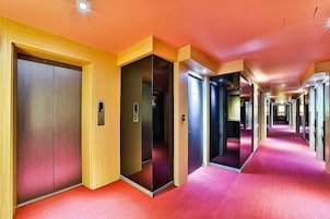 A hotel corridor with multiple doors, red carpet flooring, and wooden paneling on the walls.