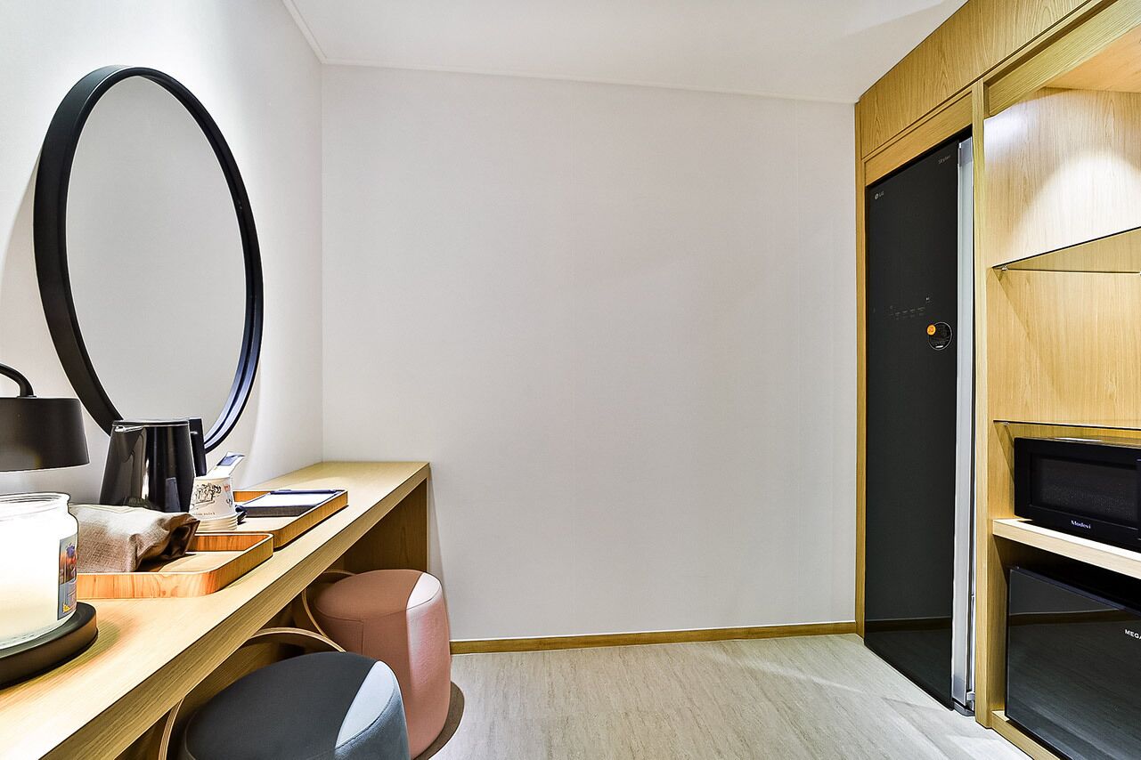 Habitación de hotel moderna con un escritorio de madera, un espejo grande, un televisor y un armario.