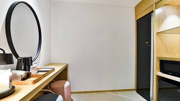 Habitación de hotel moderna con un escritorio de madera, un espejo grande, un televisor y un armario.