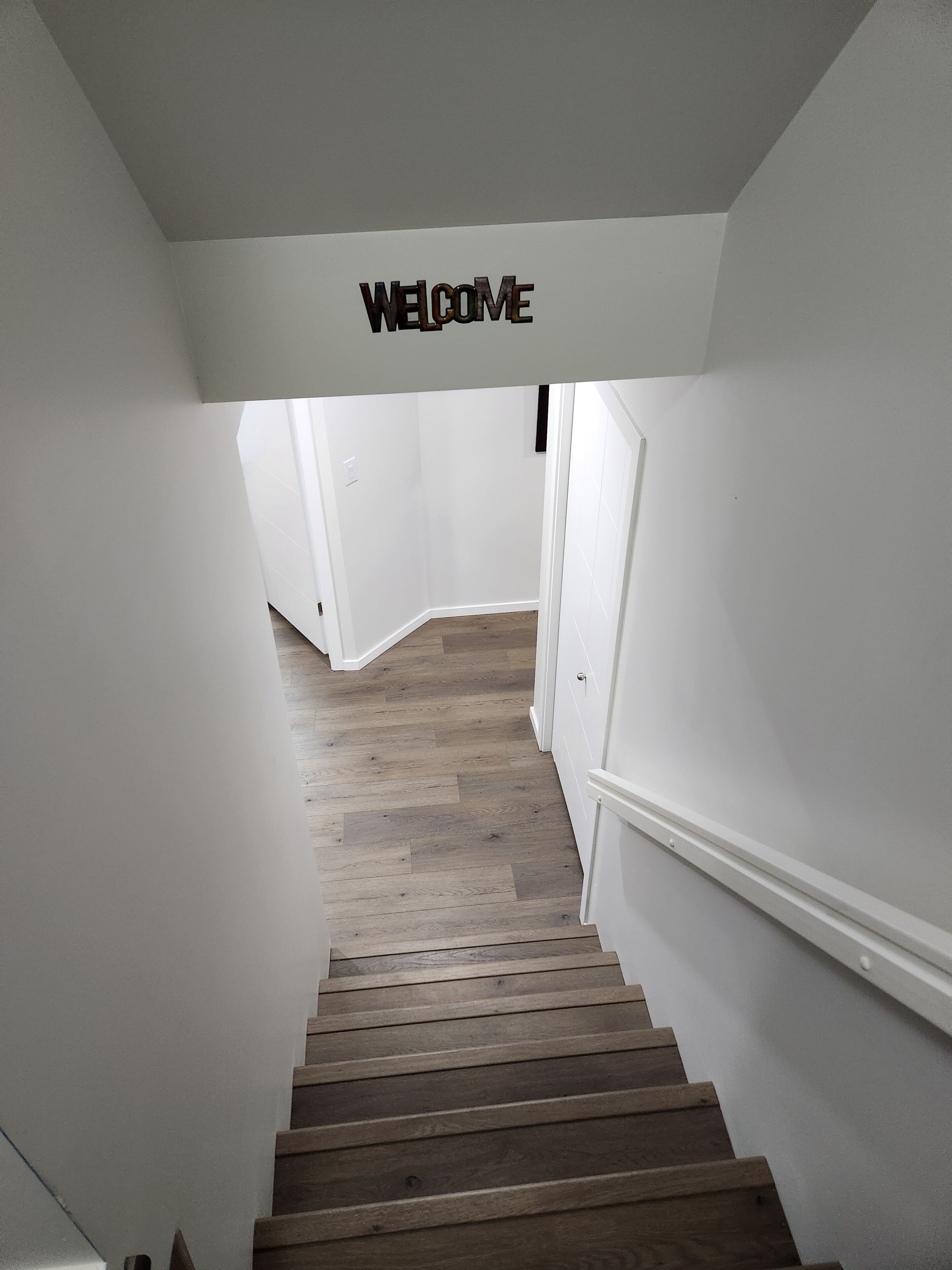 A staircase with a 'WELCOME' sign above it, leading to a room with white walls and wooden flooring.