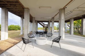 Un espace extérieur aménagé avec une table ronde et des chaises, des piliers en béton et une partie abritée avec un escalier.