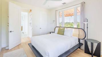 A bedroom with a bed, a ceiling fan, a window with curtains, and a bedside table.
