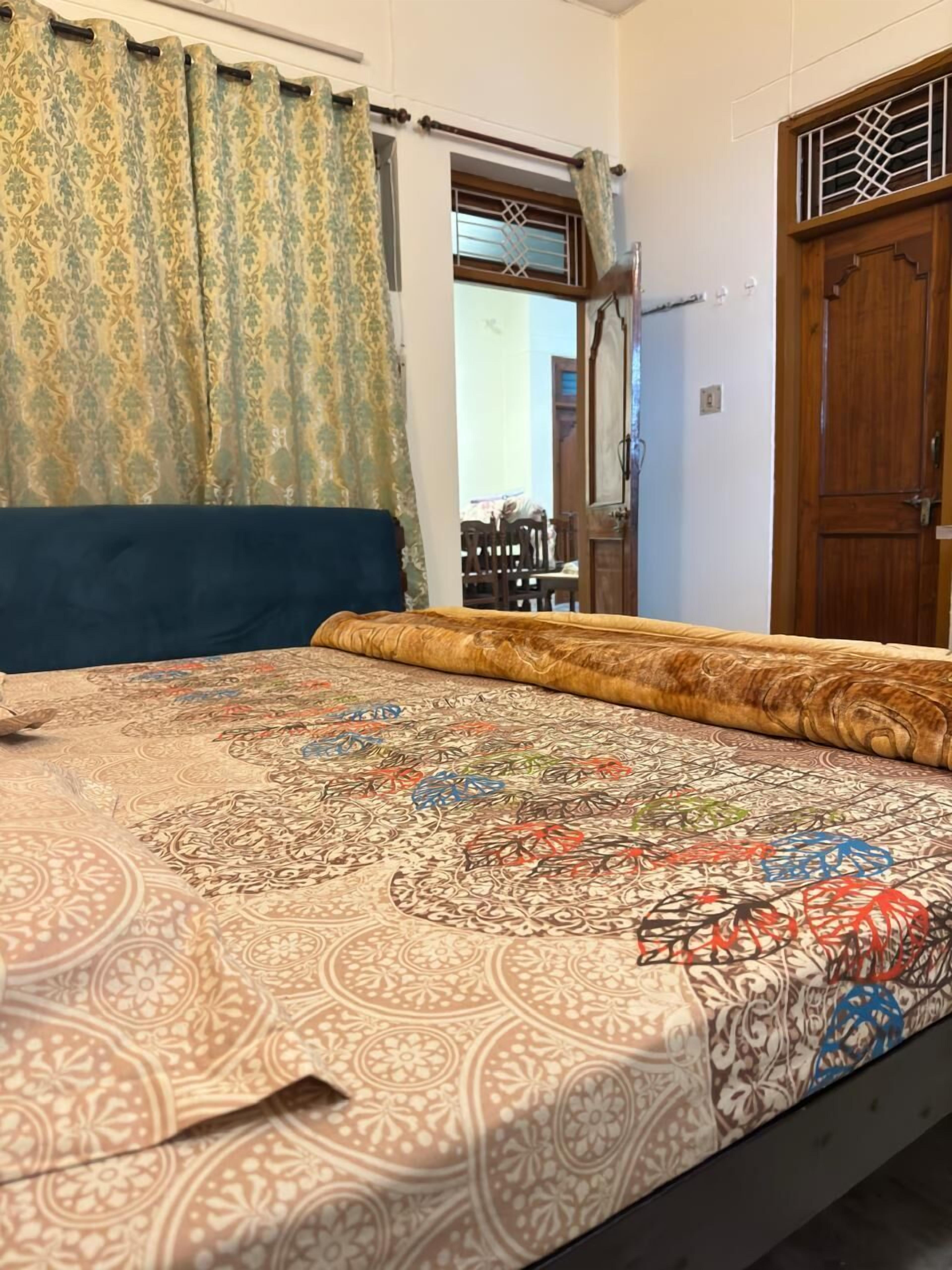Un dormitorio con una colcha estampada, una puerta de madera y una ventana con cortinas.
