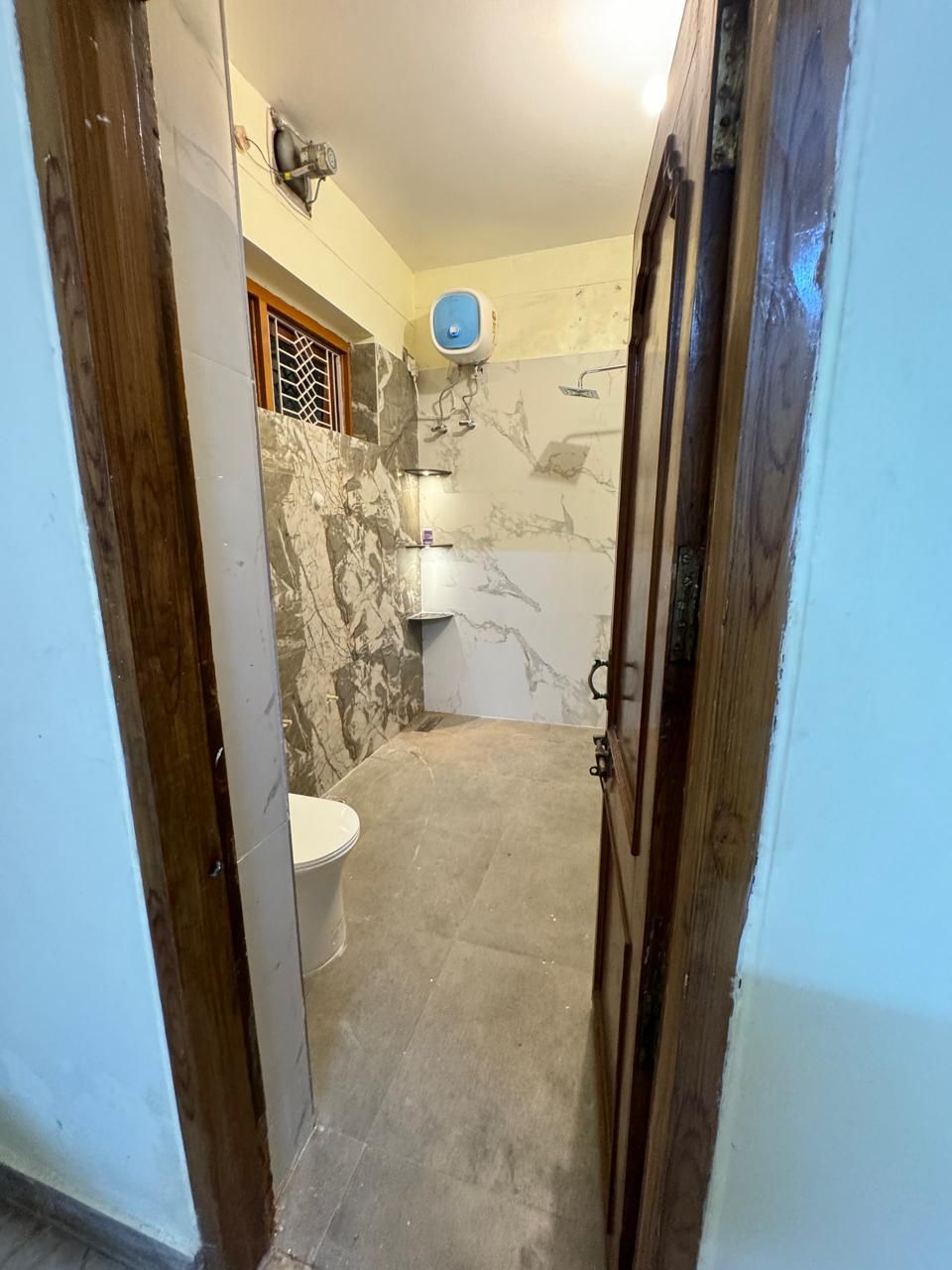 Un baño estrecho con inodoro, ducha y pared de mármol.