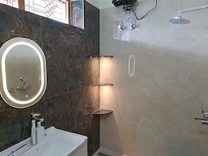 A modern bathroom with a large oval mirror, a white sink, a handheld showerhead, and a wall-mounted toilet. - Mishra's Bungalow (Prayagraj)