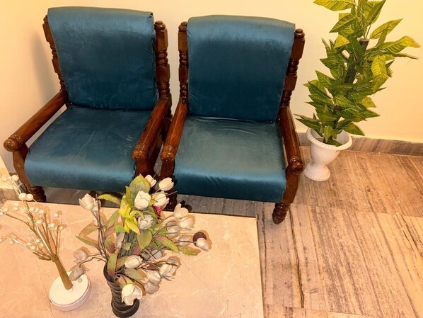 Dos sillones tapizados en azul con estructura de madera, un florero con flores y una planta en maceta.