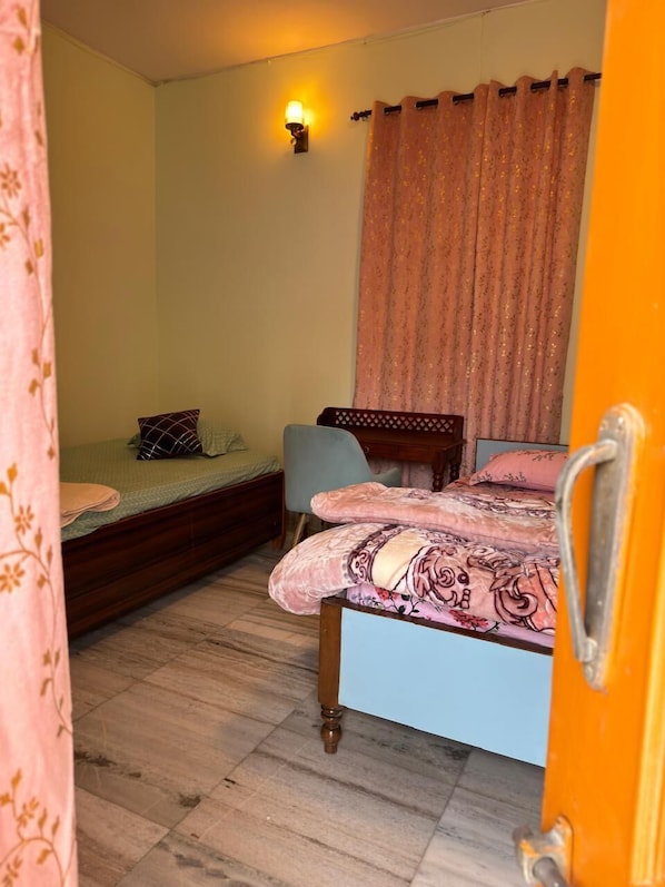 A bedroom with a bed, a chair, a desk, and a wall-mounted light fixture. - Mishra's Bungalow (Prayagraj)