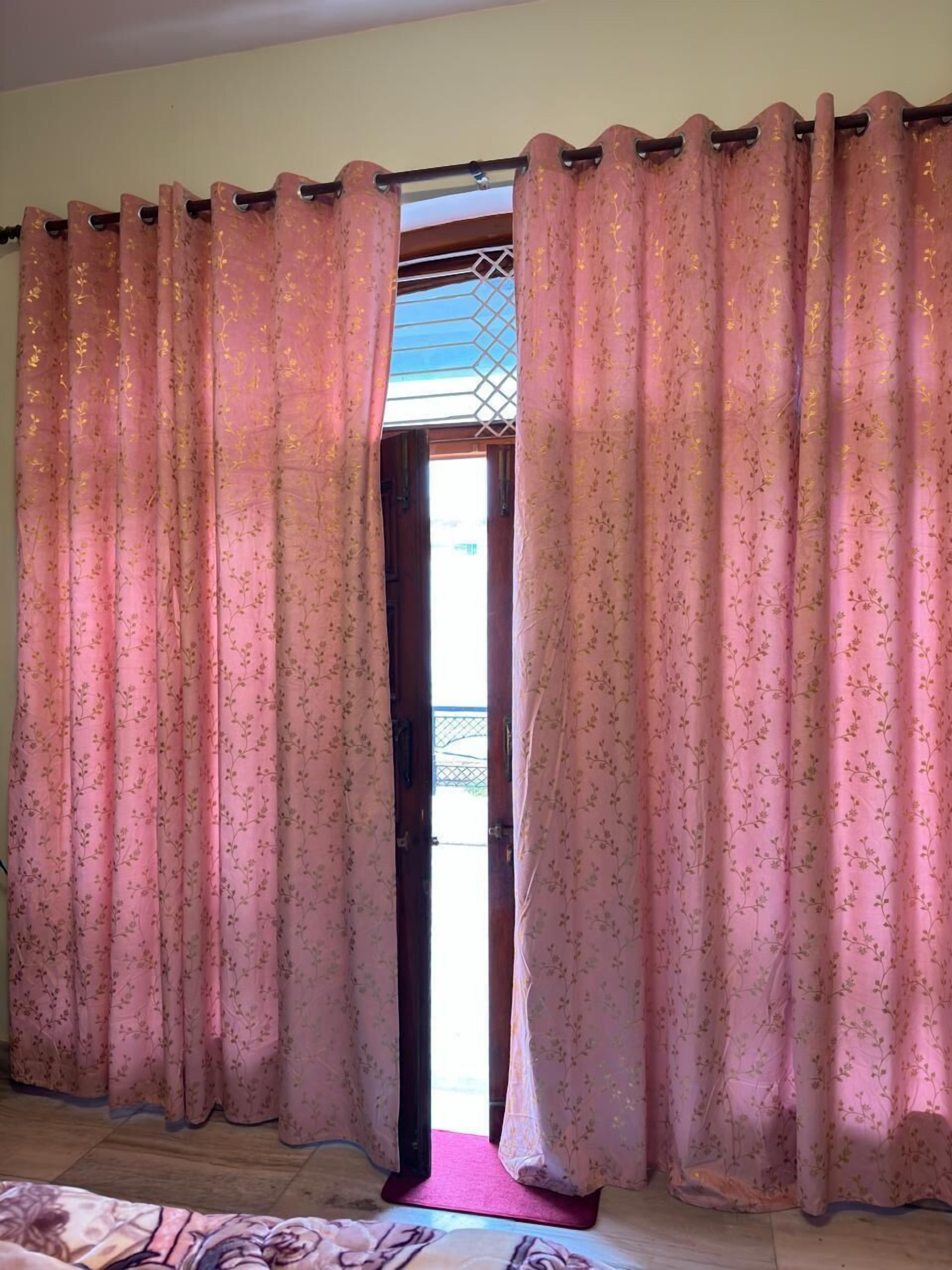 A room with pink floral curtains, a wooden floor, and a view through a window with a metal grid.