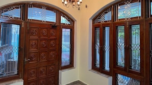 A hallway with two wooden doors with intricate designs and metal bars, a chandelier, and an air conditioning unit on the wall.