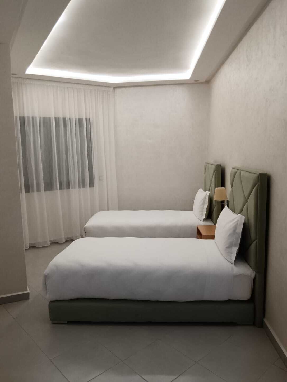 A modern hotel room with a skylight, two single beds, a nightstand, and a lamp.