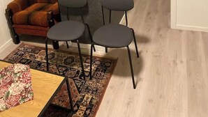 Une pièce comprenant un fauteuil en cuir marron, une petite table et trois chaises noires. Un tapis à motifs recouvre le sol.