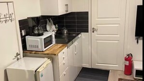 Une cuisine compacte avec des meubles blancs, un four à micro-ondes, un petit réfrigérateur et un crédence noire en carreaux.