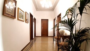 A hallway with framed artwork on the walls, a chandelier, a wooden door at the end, and a dining area with chairs and a table. - Spacious apartment in classic style 200 meters from the historical center (Firenze)