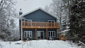 Una casa de dos pisos con un balcón de madera, rodeada de árboles cubiertos de nieve.