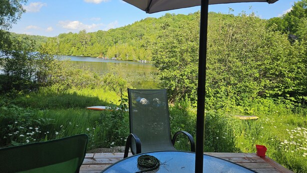 Un espacio al aire libre con una mesa y sillas, con vista a un lago y colinas boscosas.